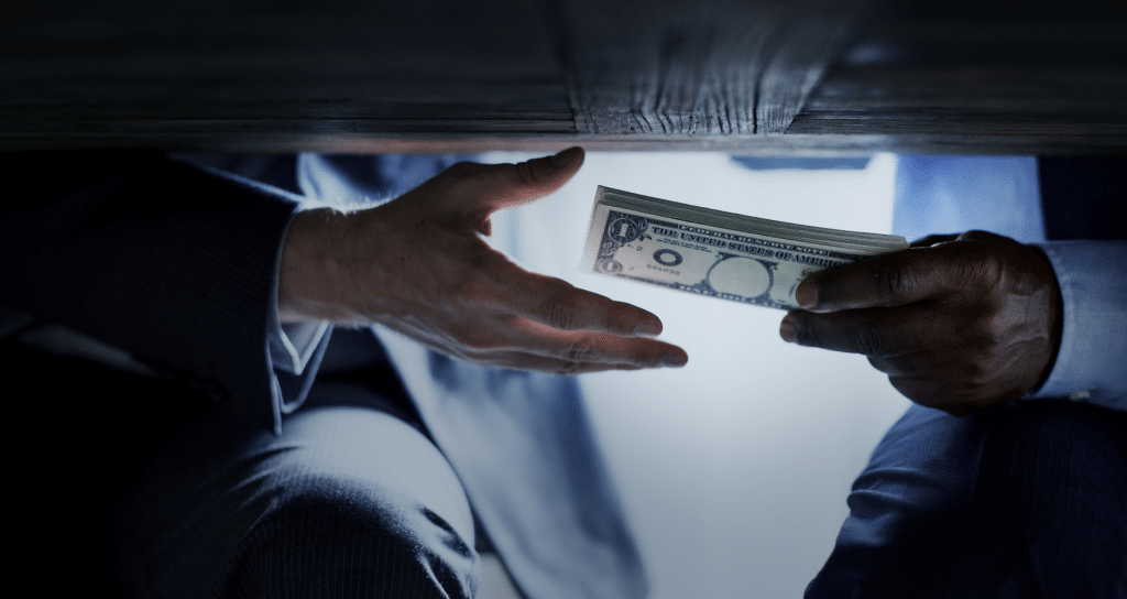 Two men handing cash to each other under a table.