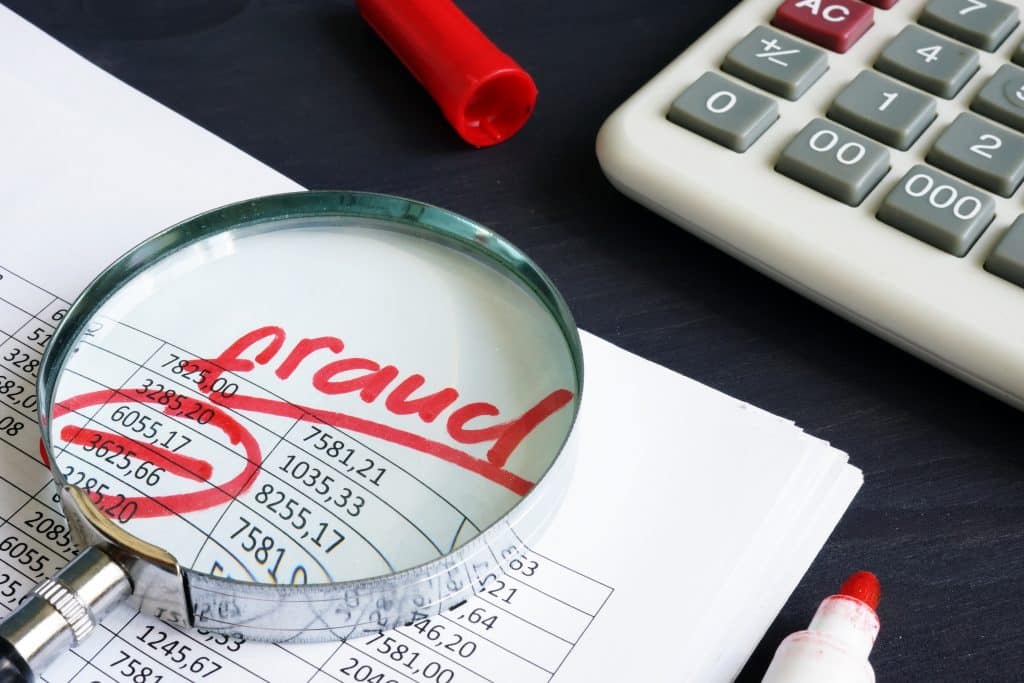 A magnifying glass sitting on a piece of paper focusing on the word Fraud in red writing